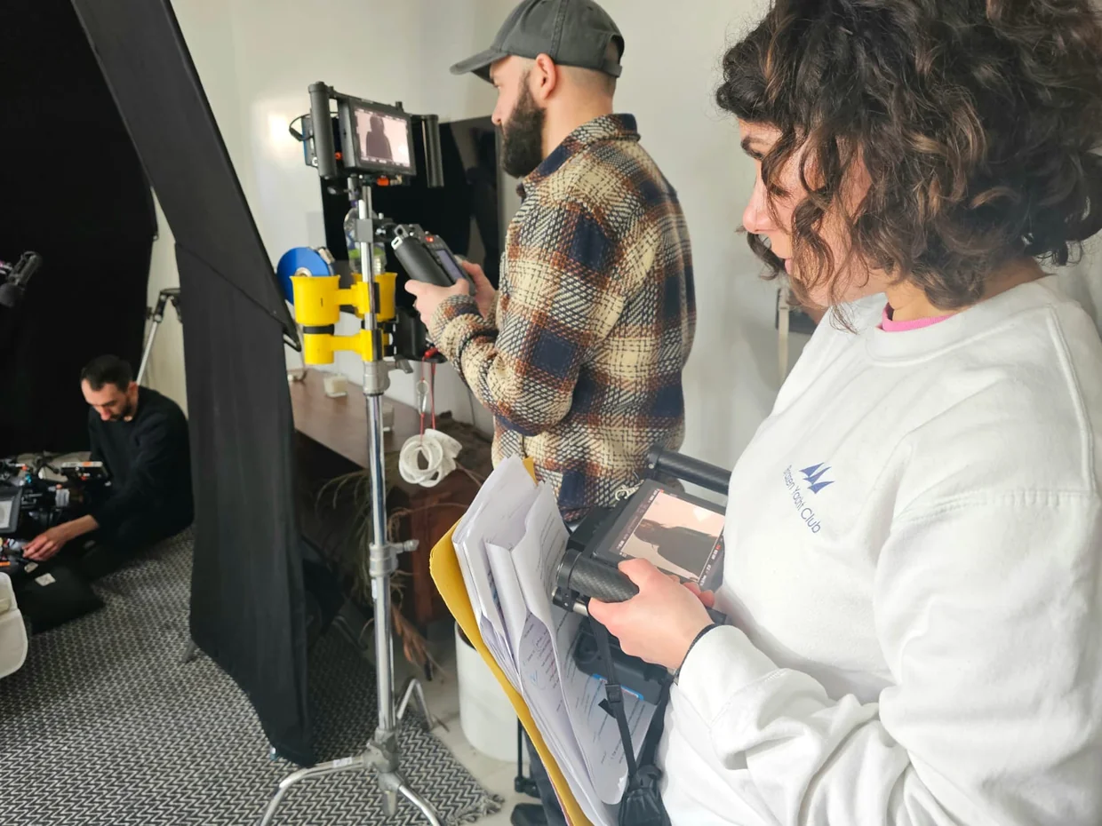 Farah Halime Hope reviewing a handheld monitor on set, with script pages beside her.